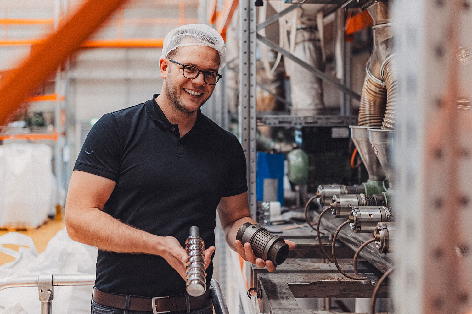Mann mit Haarnetz hält zwei Metallteile in einer Produktionshalle der Ölmühle Solling